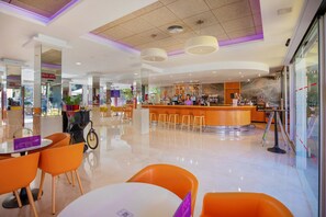 Una hall d'albergo moderna con un'area bar centrale, diverse disposizioni di posti a sedere e un pavimento pulito e lucido.