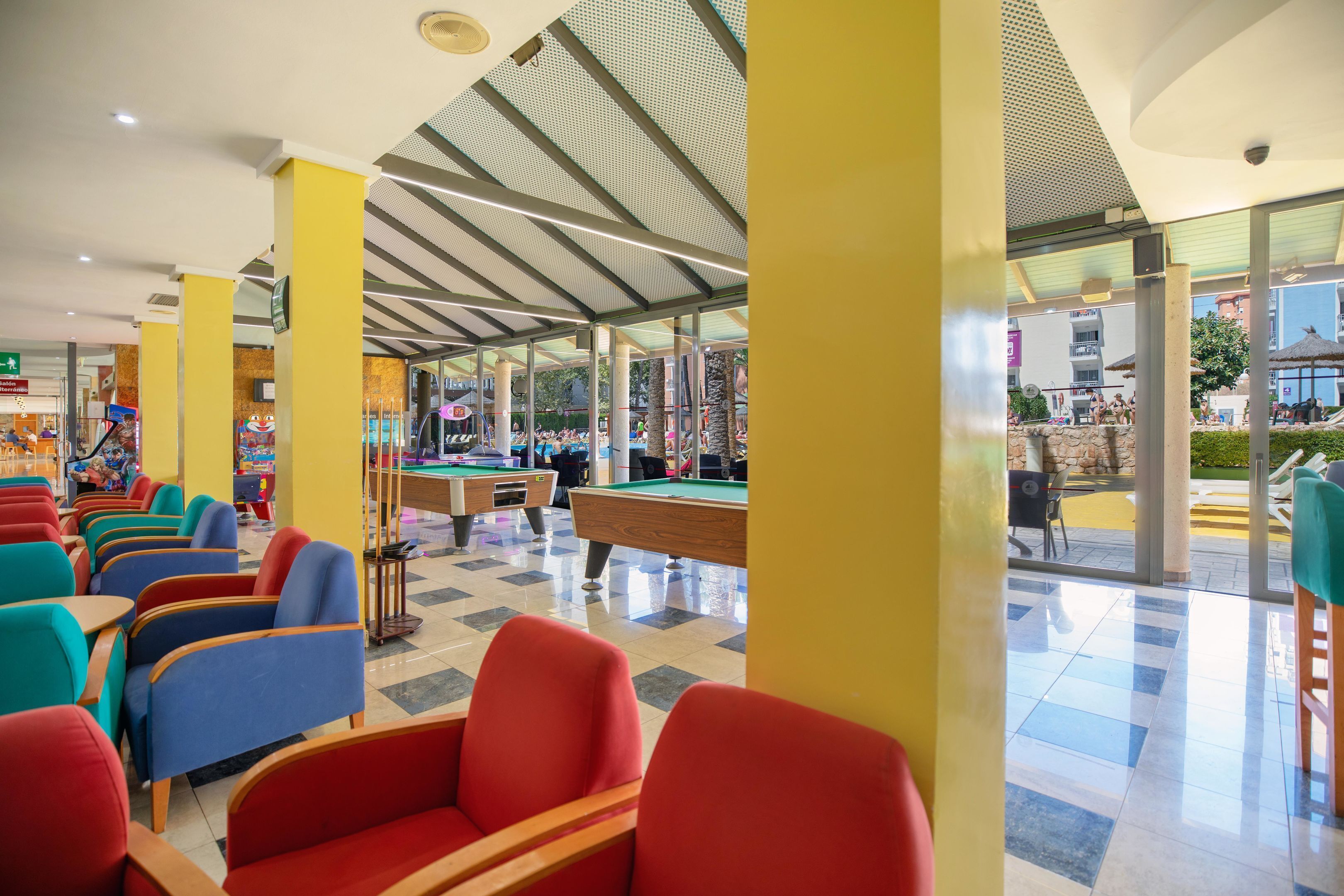 A pool table area with red and blue chairs, a pool table, and a ceiling with a geometric pattern.