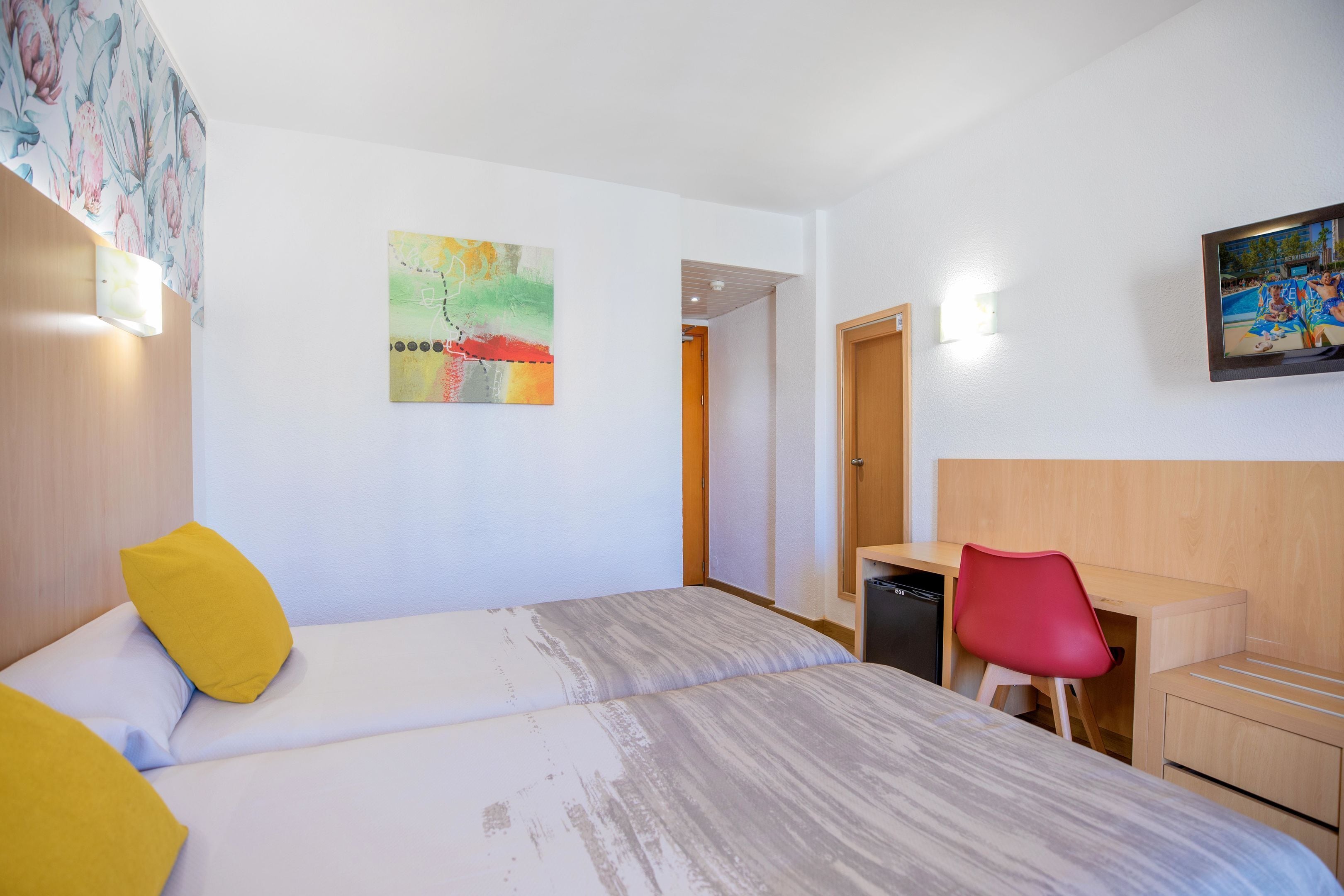 A hotel room with a bed, a desk, a chair, and a painting on the wall.