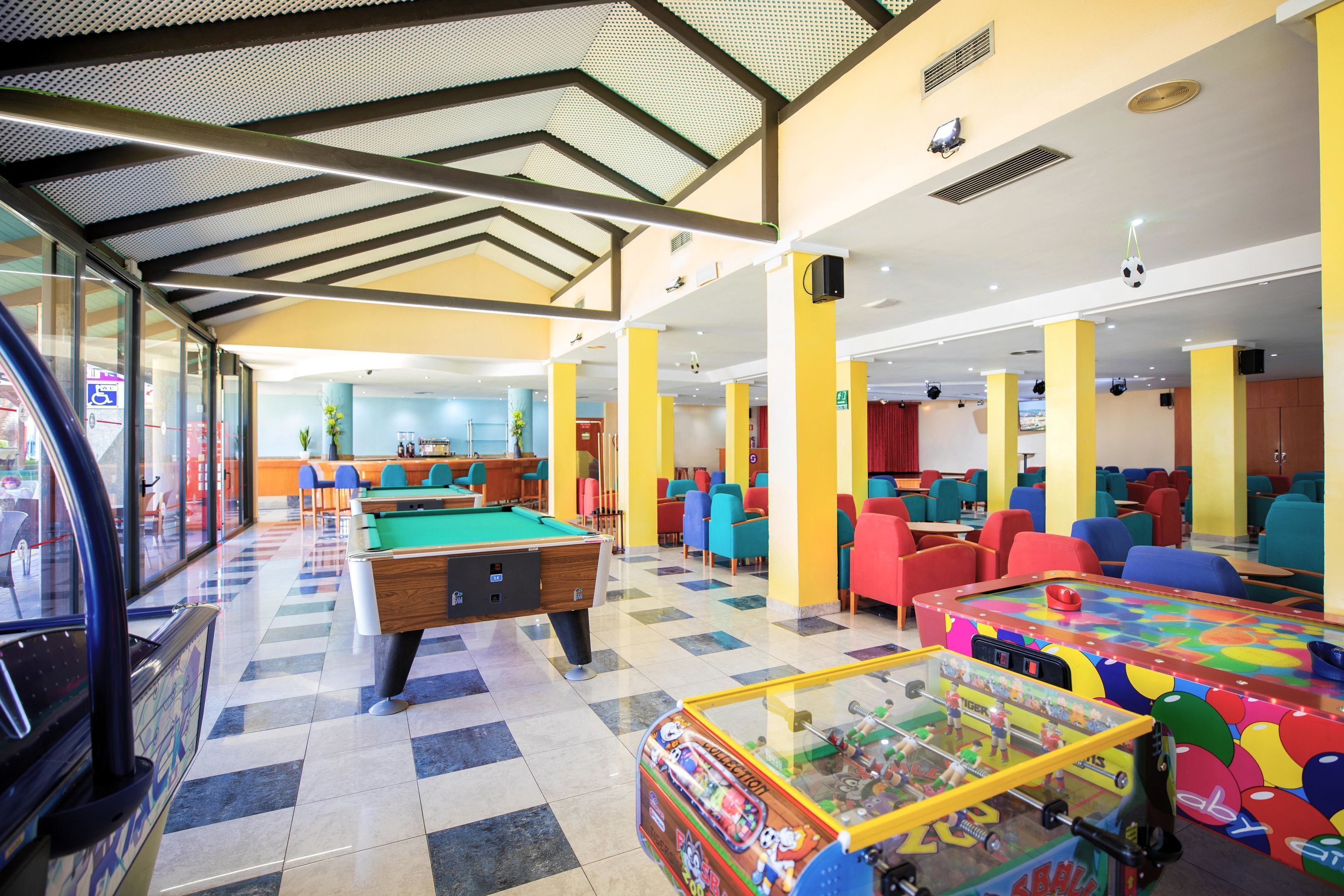 Zona interior i ben il·luminada de lleure amb taules de bitlles, taula de futbolí i seients de colors.