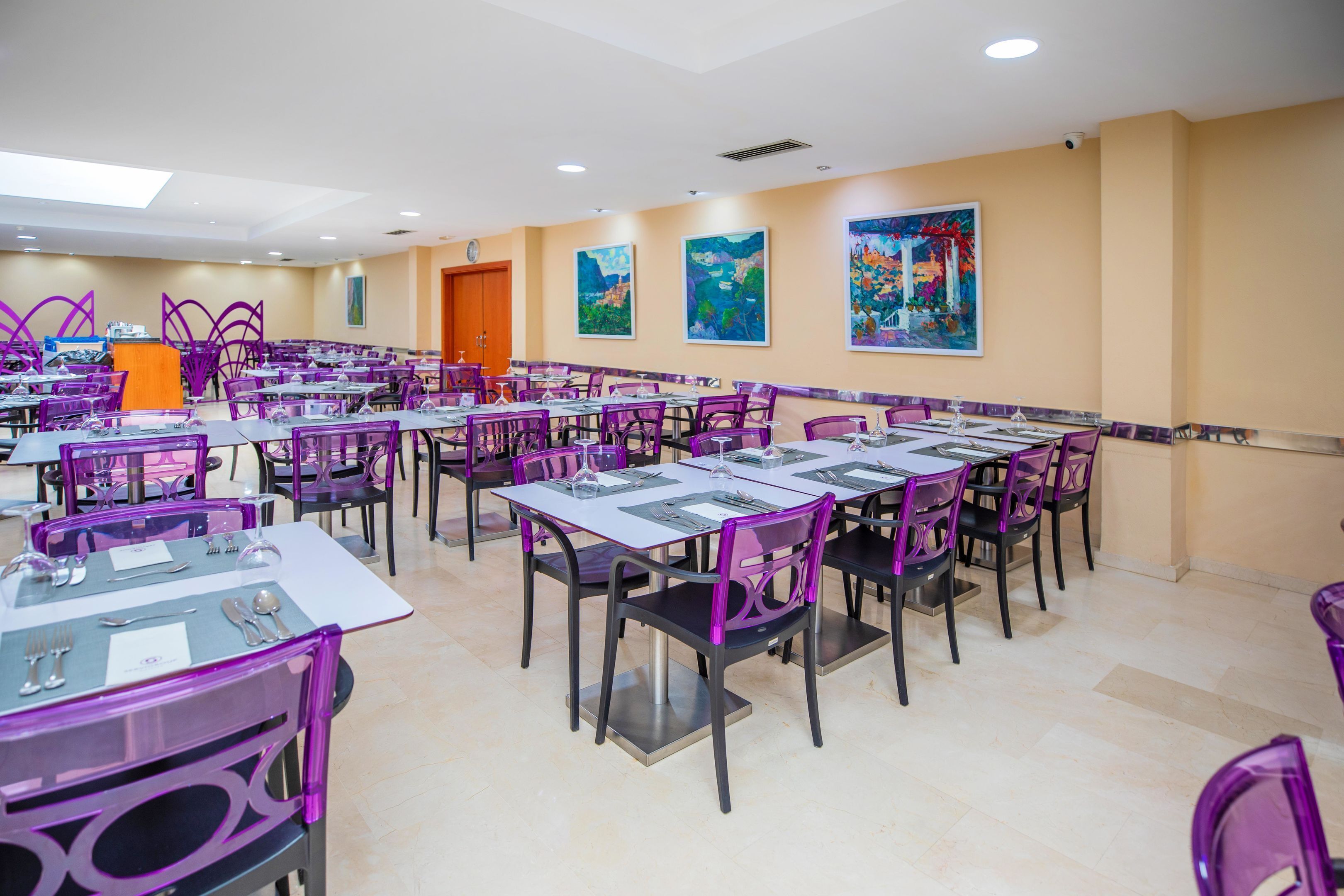 Un área de comedor con varias mesas y sillas, un atril y obras de arte en las paredes.