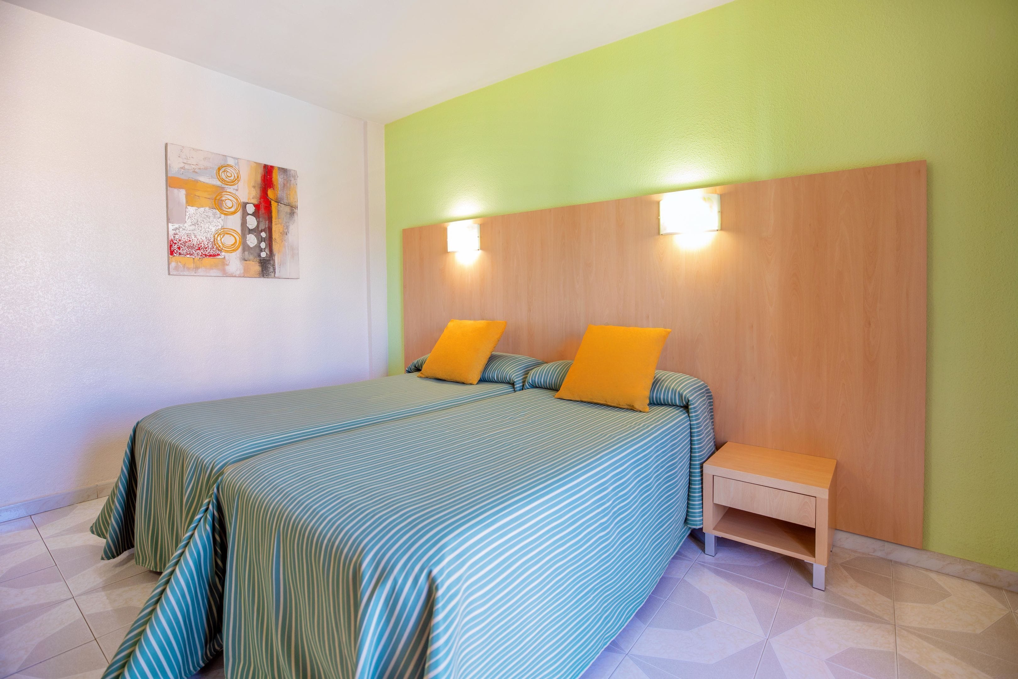 A bedroom with a bed, bedside table, and a wall-mounted light fixture.