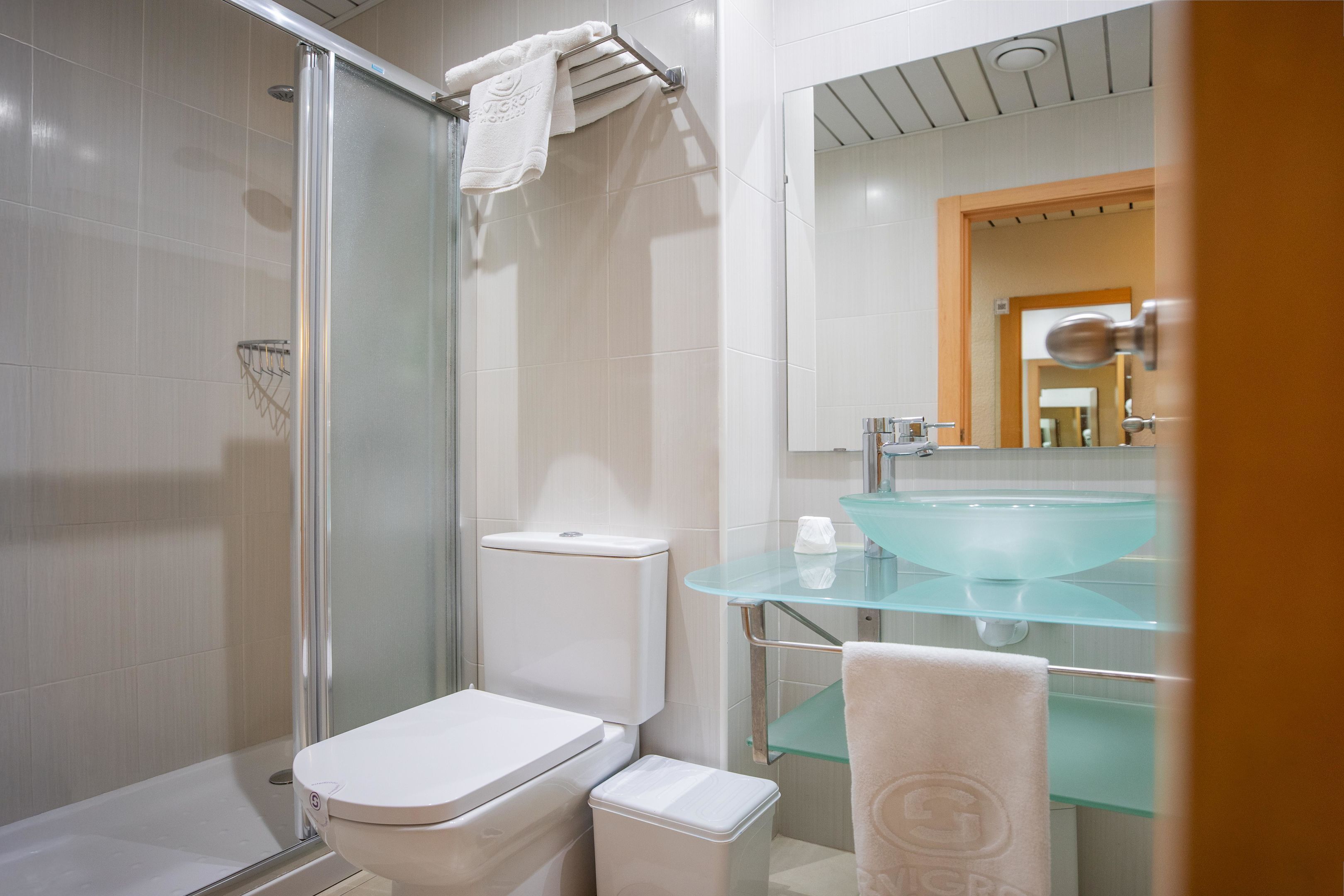 A modern bathroom with a glass shower enclosure, a white toilet, and a glass sink with a chrome faucet.