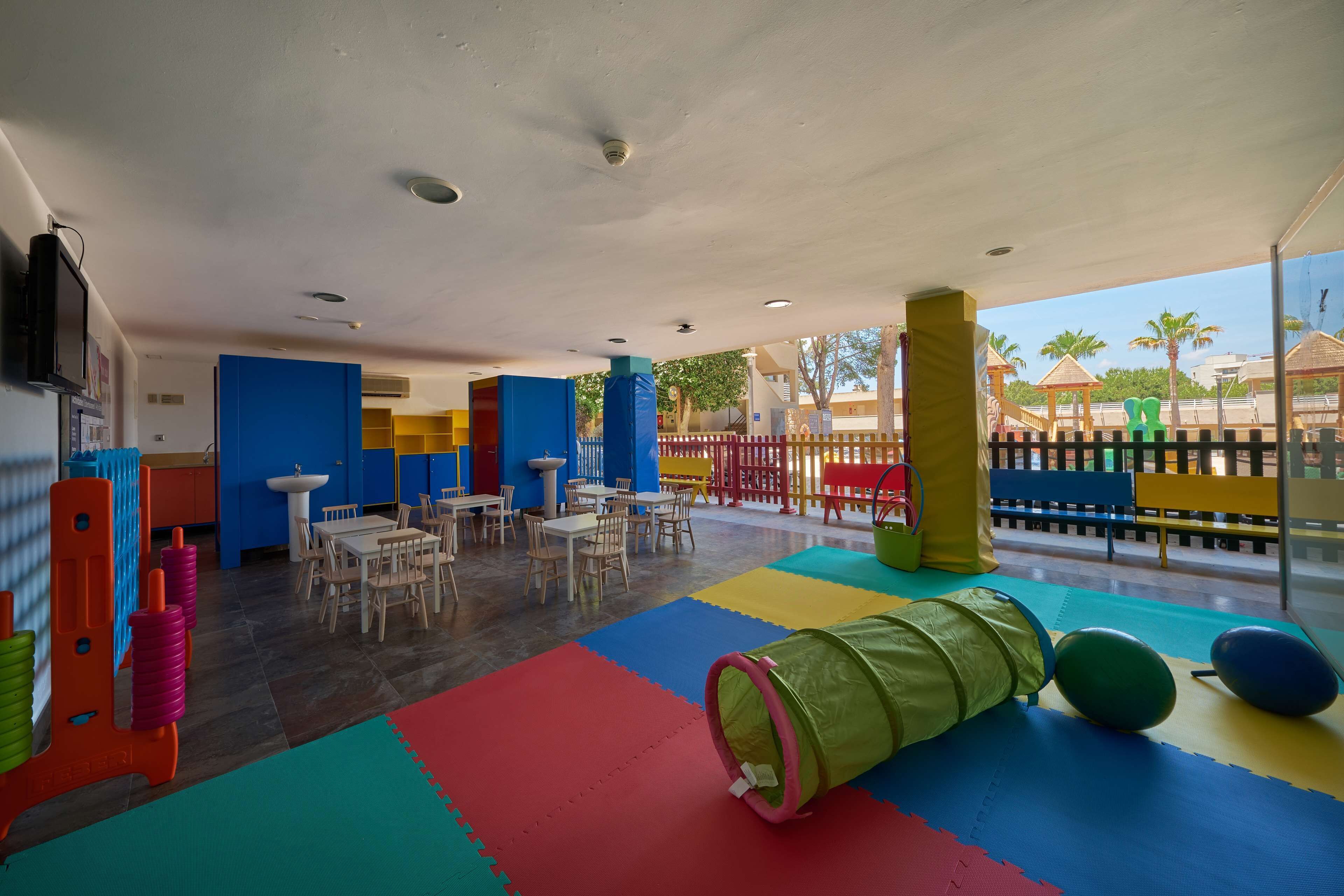 Een speelruimte voor kinderen met kleurrijke matten, speeltoestellen en tafels.