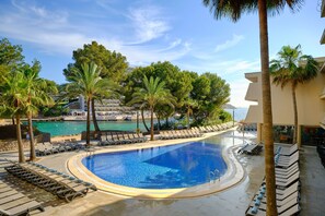 Una piscina con sillones de descanso, palmeras y vistas al mar.