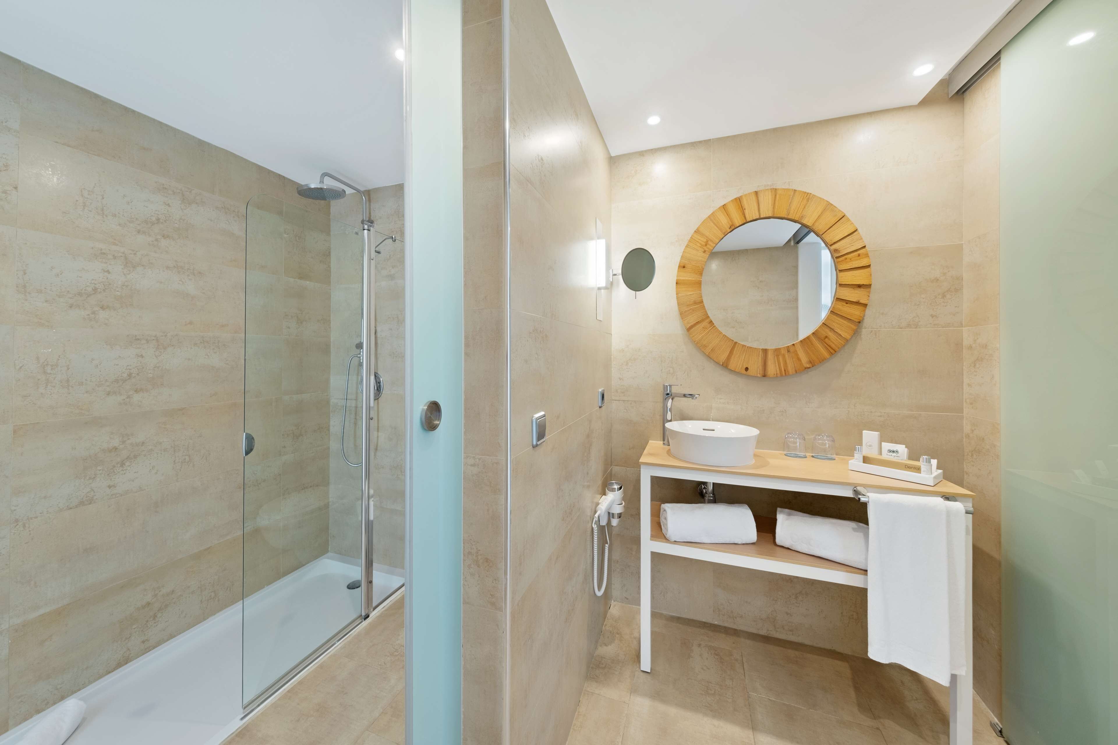 Een moderne badkamer met een douche met glazen wanden, een ronde spiegel en een witte wastafel met een houten blad.
