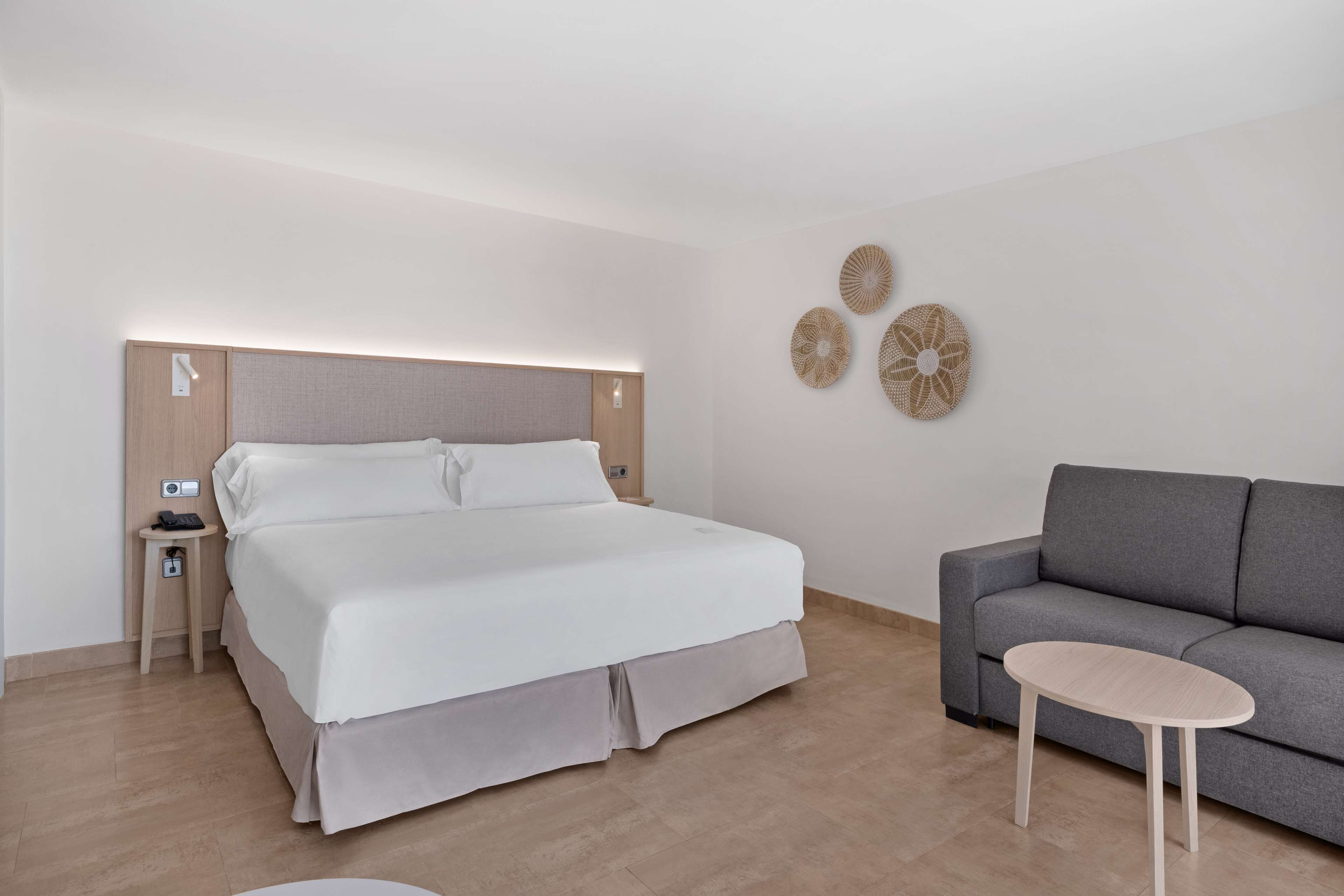 A modern hotel room with a large bed, a gray sofa, and a small round table.