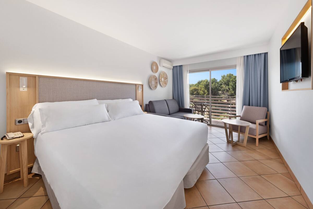 A hotel room with a large bed, a desk with a phone, a seating area with a table and chairs, and a TV mounted on the wall.