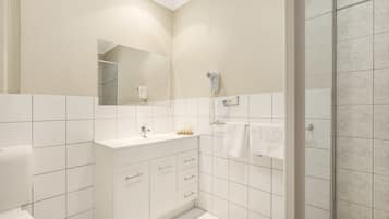 Un baño moderno con baldosas blancas, un lavabo, un espejo, un secador de pelo y una ducha.