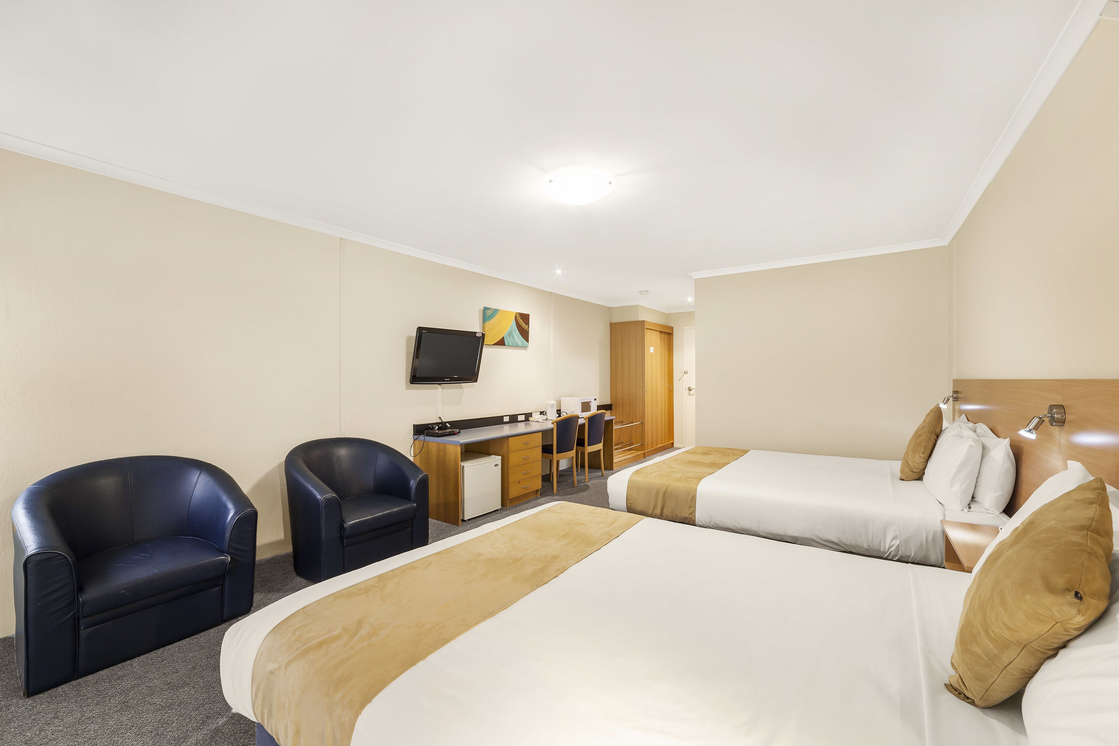 A hotel room with two beds, a desk, chairs, and a television.