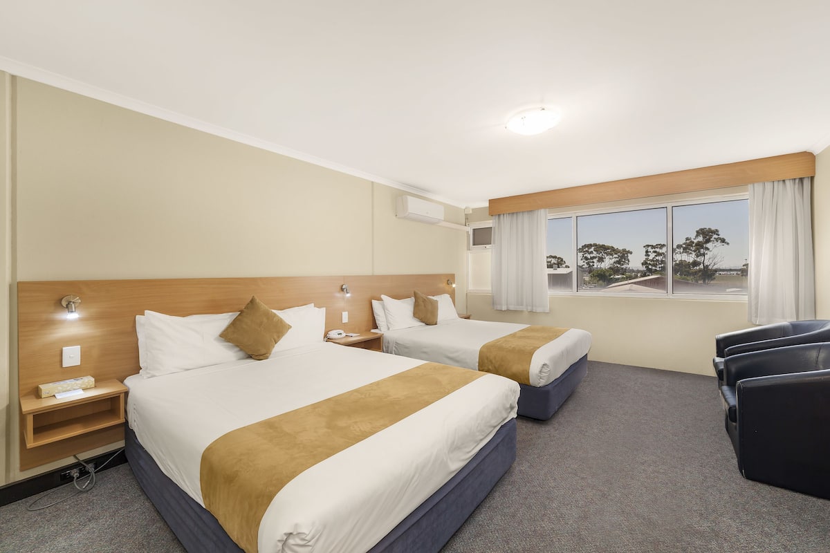 Ein Hotelzimmer mit zwei Betten, einem Schreibtisch, einem Sessel und einem großen Fenster mit Blick.