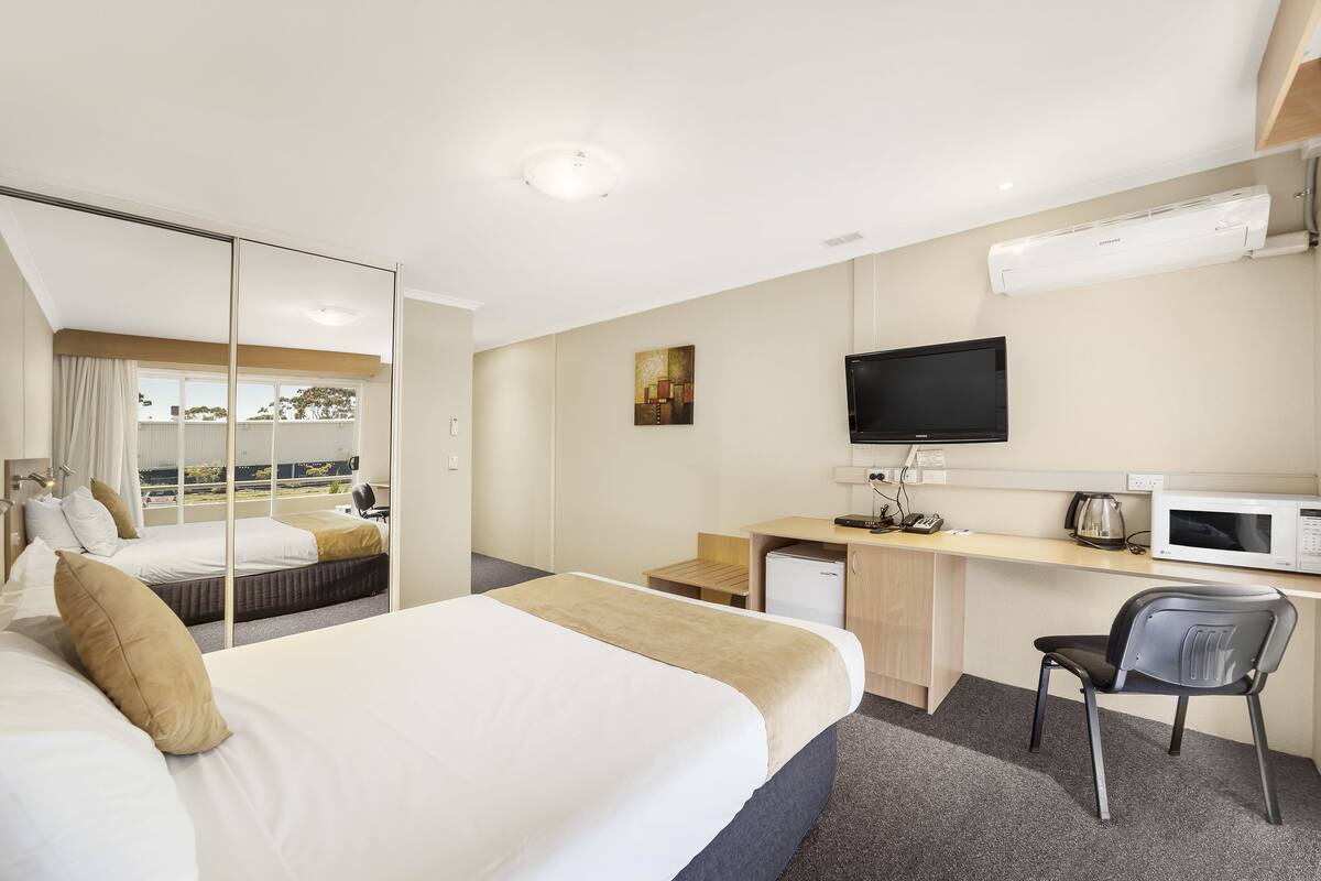 Ein Hotelzimmer mit Bett, Schreibtisch, Stuhl, Fernseher und Blick ins Freie.