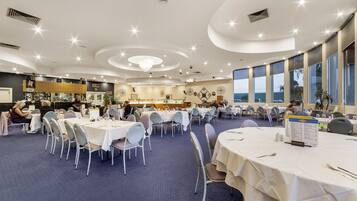 Un comedor amplio con mesas y sillas redondas, una barra al fondo y ventanas grandes con vistas.
