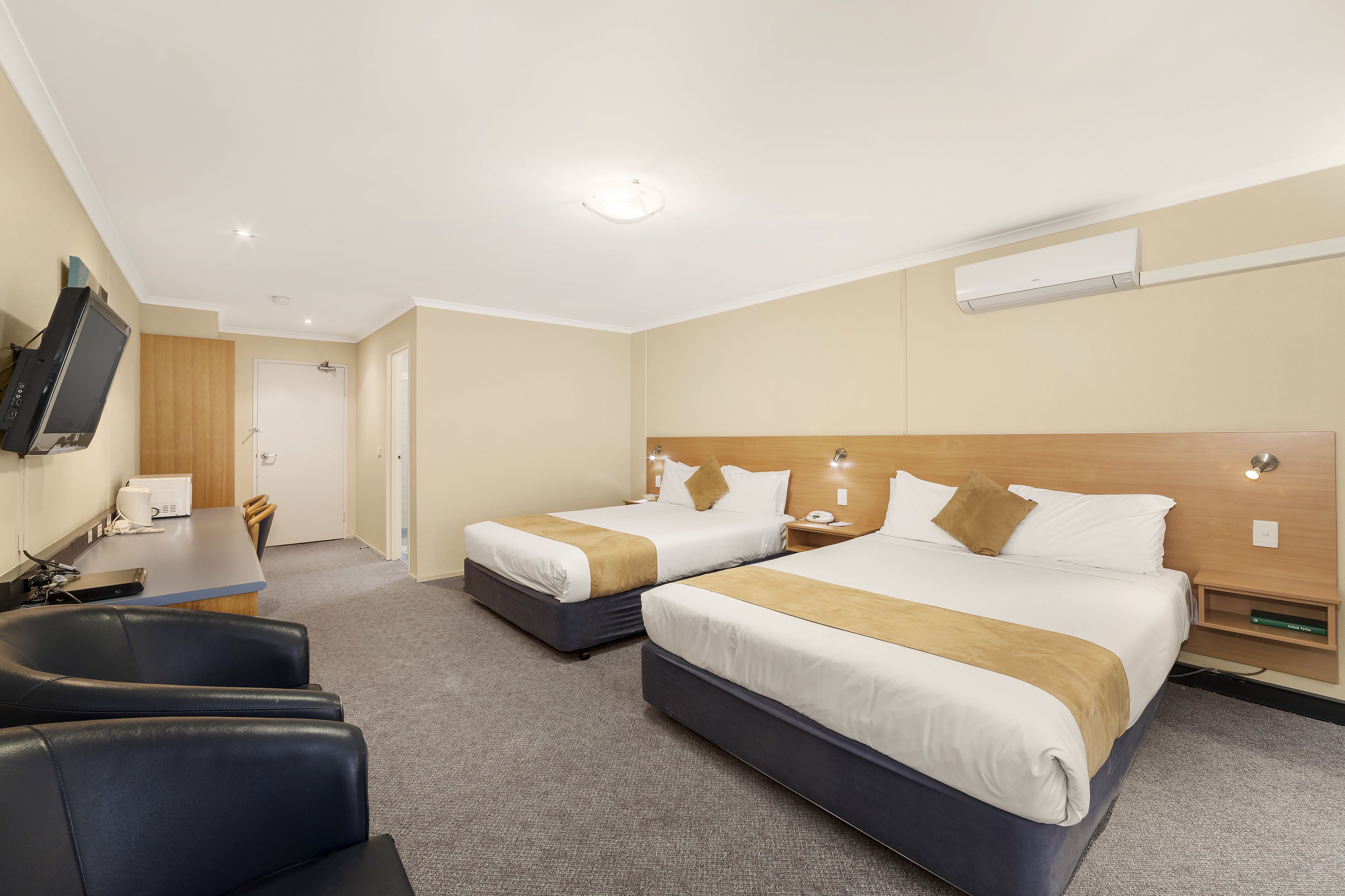 A hotel room with two beds, a desk, a chair, and a TV.