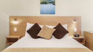 Ein ordentlich bezogenes Bett mit Holz-Kopfteil, zwei Nachttischen und einer Wandleuchte.