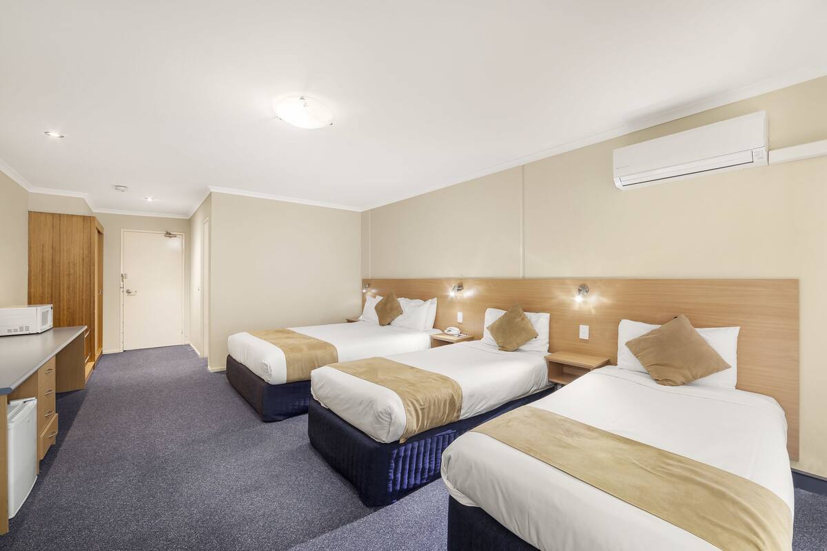 Ein Hotelzimmer mit drei Betten, einem Schreibtisch, einer Mikrowelle und einer Klimaanlage.