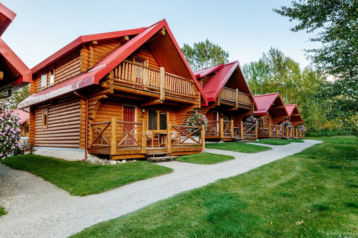 Una hilera de cabañas de madera con techos rojos y balcones de madera, rodeadas de un césped cuidado y árboles.