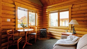 A cozy cabin interior with wooden walls, a round table with chairs, a fireplace, and a sofa with a blanket. - Miette Mountain Cabins (Pocahontas)