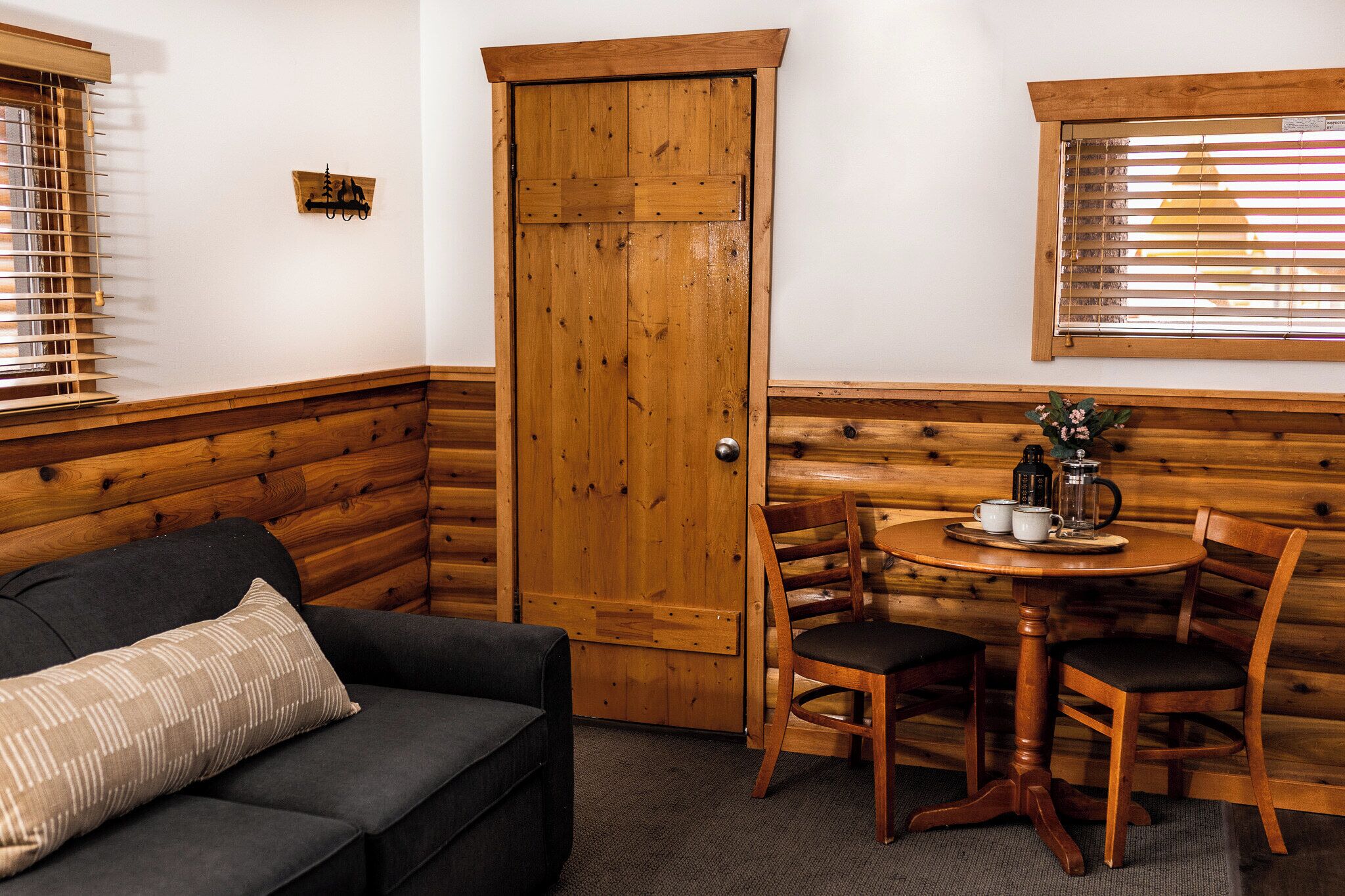 Un rincón acogedor con una puerta de madera, una pequeña mesa con sillas y un sofá con un cojín.