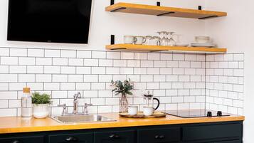 A kitchen with white tiled backsplash, a wooden countertop, a black stove, and a shelf with glassware and plates.