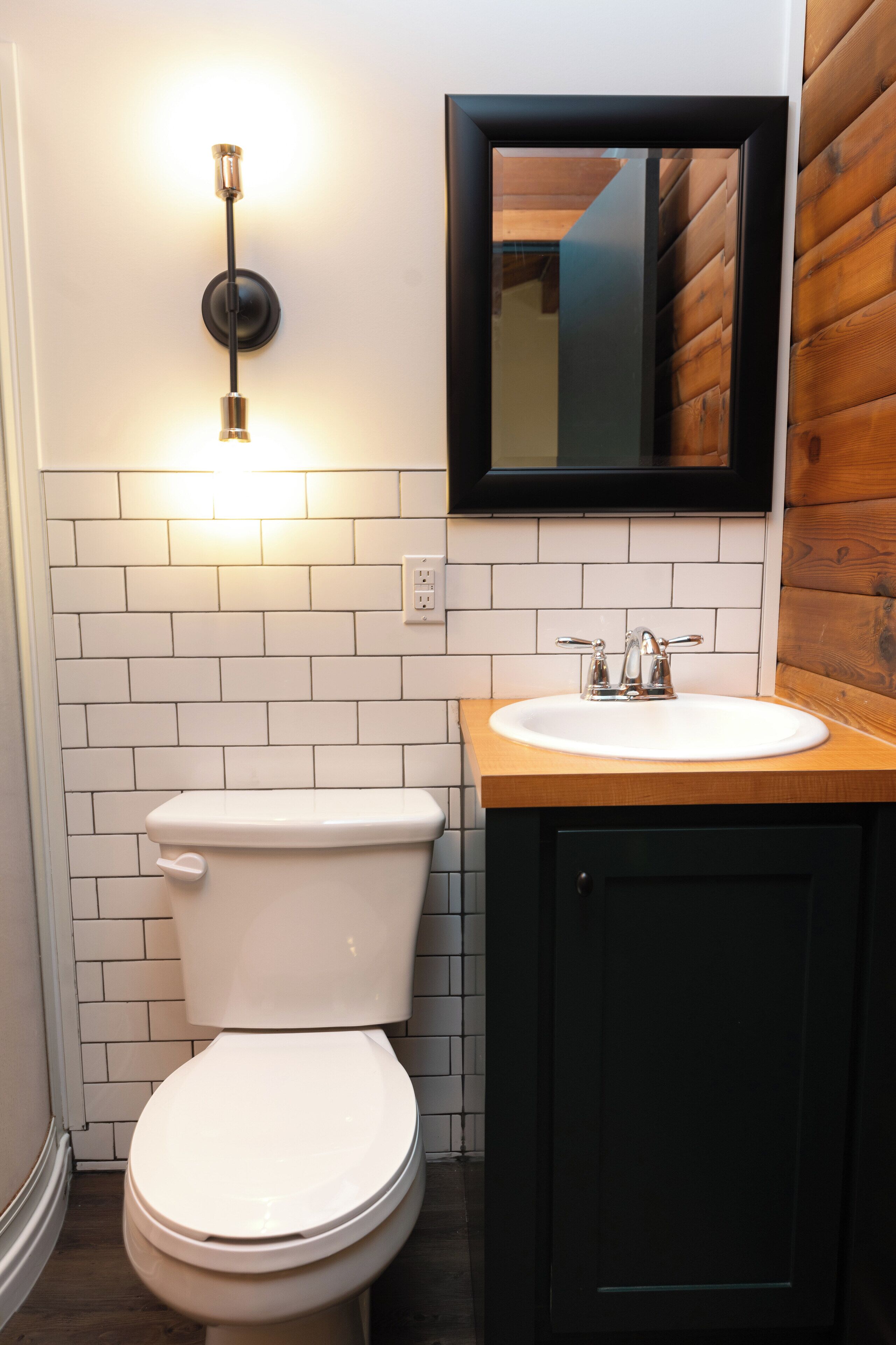 A bathroom with a white toilet, a wooden vanity with a sink, and a wall-mounted mirror.