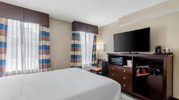 Una camera d'albergo con un letto, una televisione, una scrivania con una macchina per caffè e un minibar.