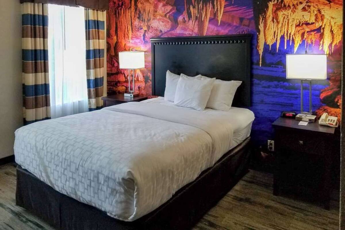 A hotel room with a large bed, striped curtains, and a wall mural of cave formations.