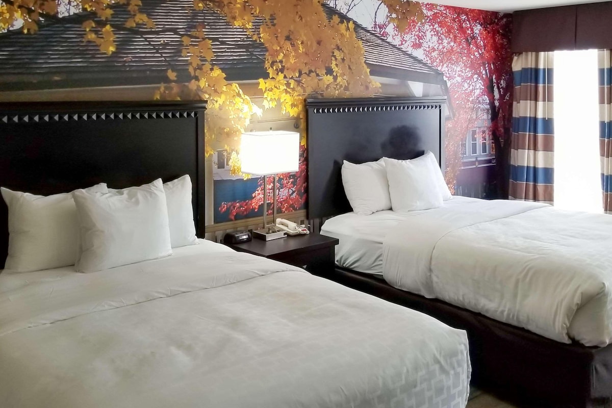 A hotel room with two beds, a nightstand with a lamp, and a painting on the wall.