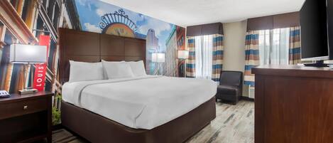 Quarto de hotel com uma cama grande, uma escrivaninha com luminária, televisão e um mural de paisagem urbana na parede.