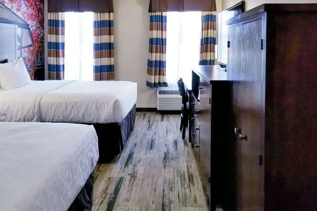 Une chambre d’hôtel avec deux lits, un bureau, une armoire et une fenêtre avec des rideaux à rayures.
