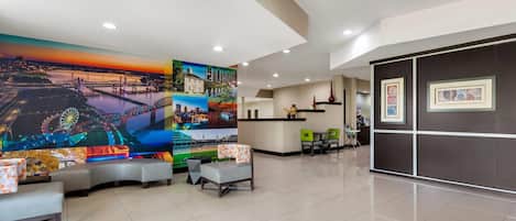 Un vestíbulo de hotel con un mural grande, una zona de estar y una recepción.