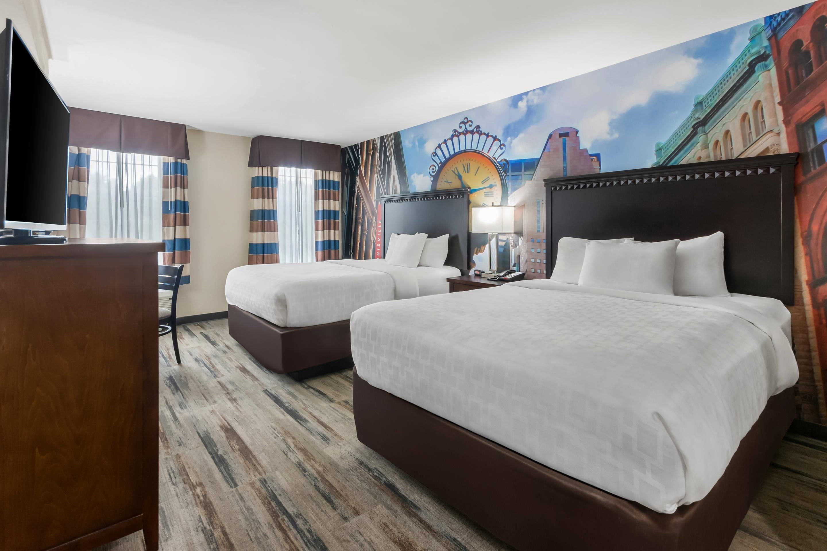Habitación de hotel con dos camas, un televisor y un mural de un paisaje urbano.