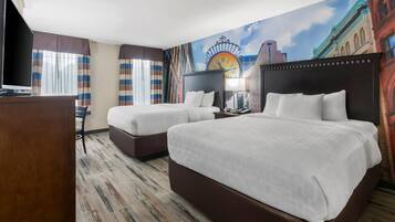 Habitación de hotel con dos camas, un televisor y un mural de un paisaje urbano.