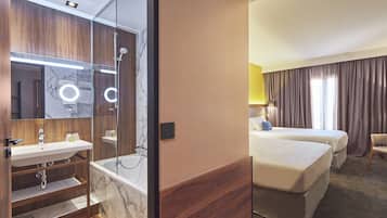 Une chambre d’hôtel avec une salle de bain comprenant un lavabo, un miroir et une douche. La chambre est équipée d’un lit et d’une chaise.