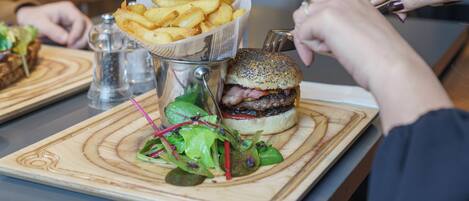Et måltid bestående af en burger, pommes frites og en salat på en træplanke.