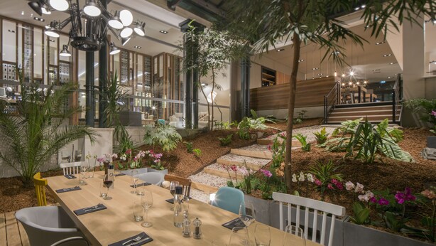 A restaurant with a long table set for dining, surrounded by indoor plants and a small garden area. - Hôtel l'Elysée Val d'Europe (Serris)