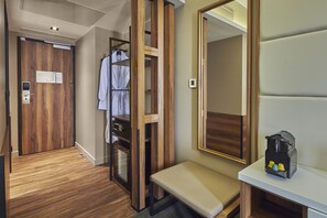 Habitación de hotel con puerta de madera, un banco, un espejo y una mesita con cafetera.