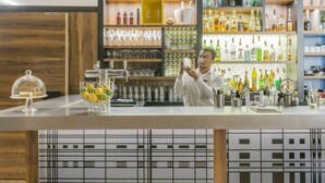 A bar area with shelves of bottles and glasses, a counter with a glass display, and a patterned wall. - Hôtel l'Elysée Val d'Europe (Serris)