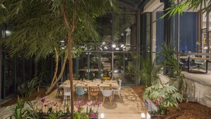 An indoor garden with a dining area, including tables and chairs, surrounded by various plants and a pathway. - Hôtel l'Elysée Val d'Europe (Serris)