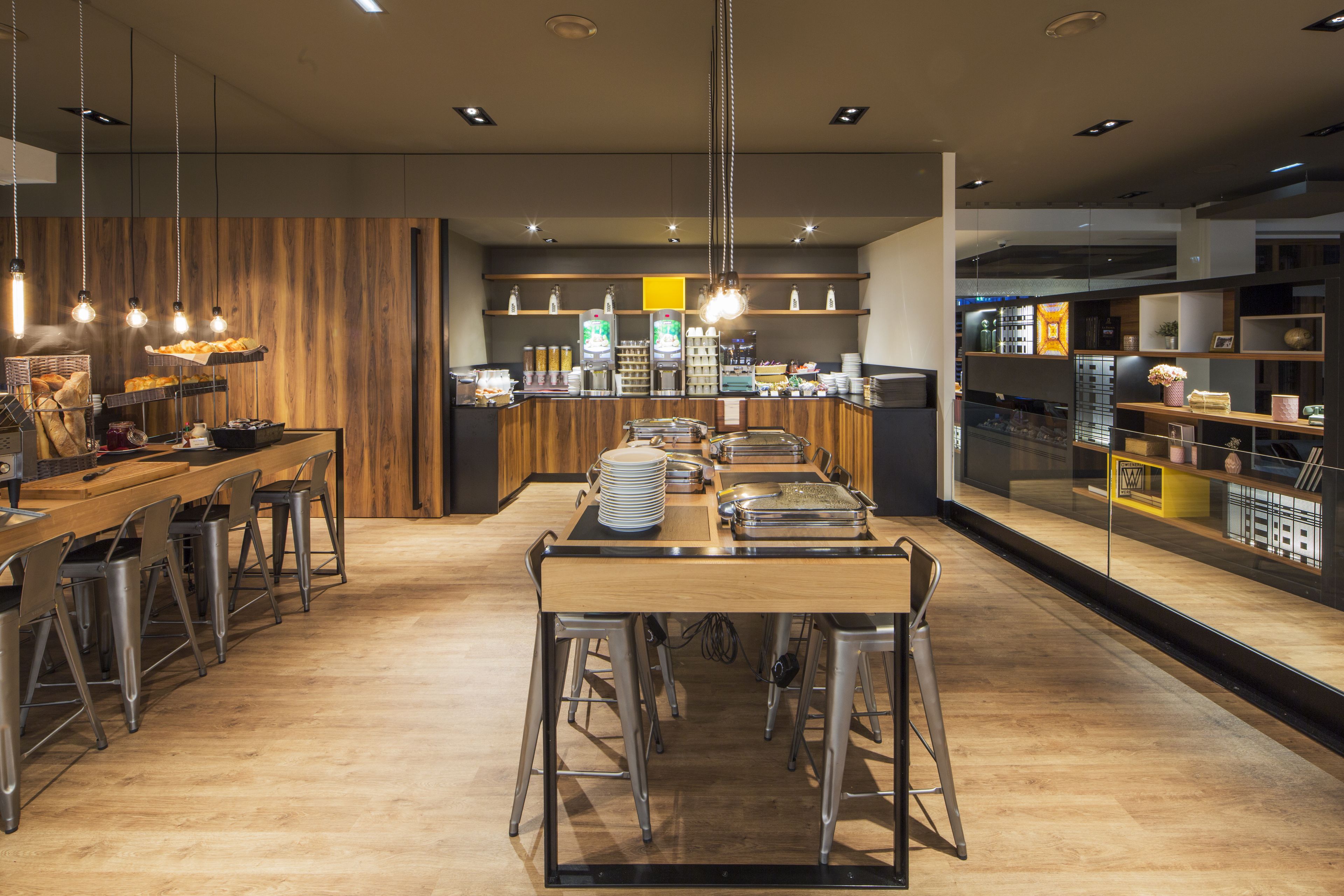 Et moderne restaurantinteriør med et centralt spisebord, barpladser samt diverse mad- og drikkepræsentationer.