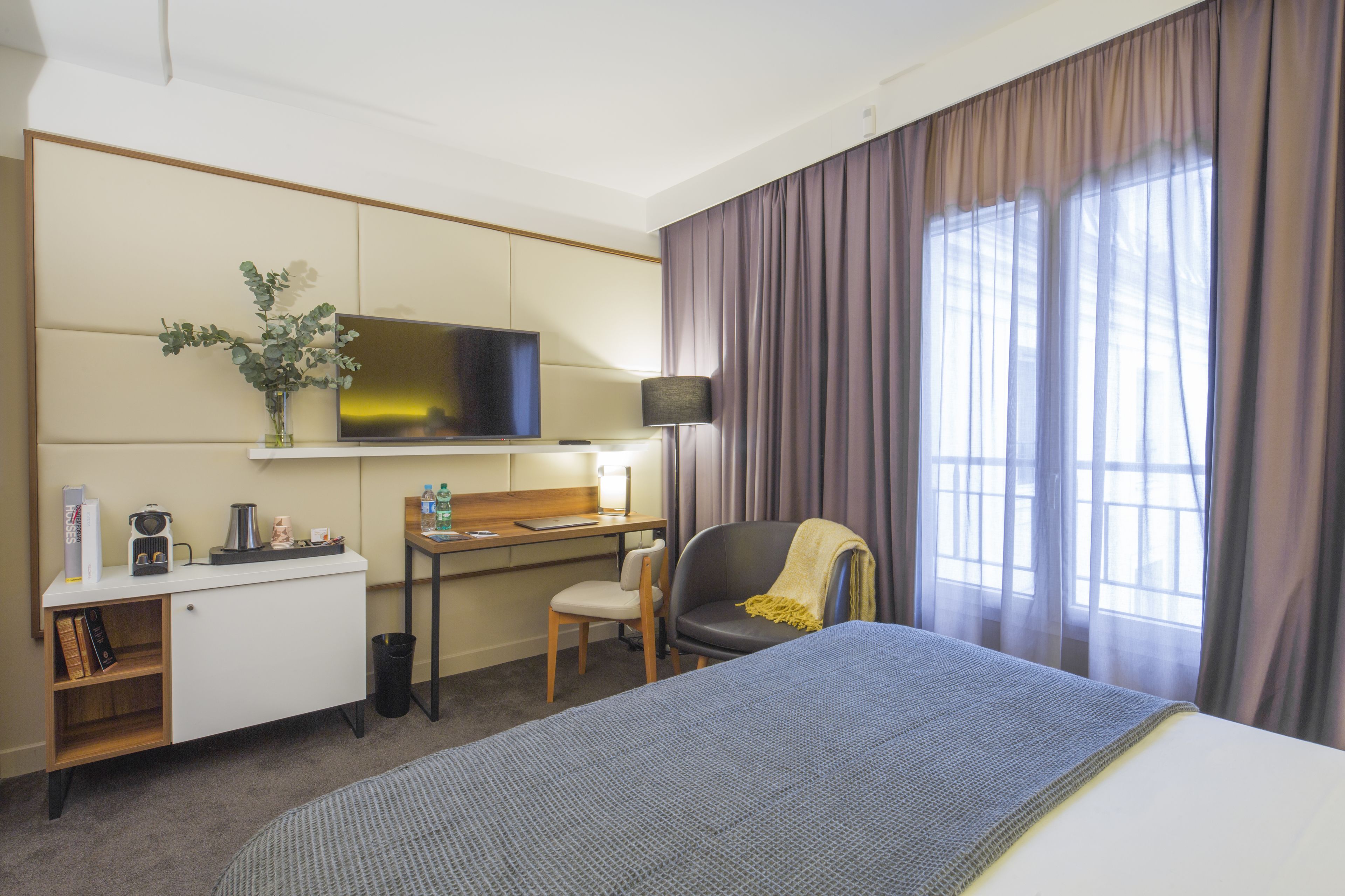 Habitación de hotel con cama, escritorio, silla, televisor y ventana con cortinas.