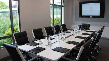 A conference room with a long table, black chairs, water bottles, and a screen displaying "Hôtel l'Elysée Val d'Europe".