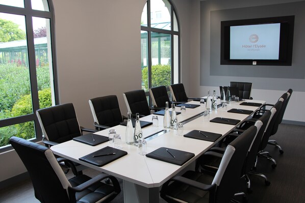 A conference room with a long table, black chairs, water bottles, and a screen displaying "Hôtel l'Elysée Val d'Europe".