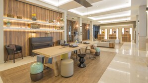A spacious, modern hotel lobby with a wooden reception desk, comfortable seating, and a large dining table. - Hôtel l'Elysée Val d'Europe (Serris)