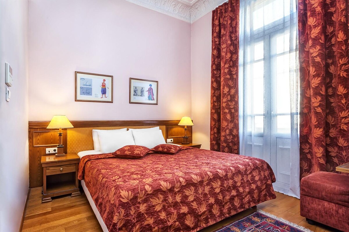 A hotel room with a large bed, two bedside tables with lamps, a wooden headboard, and two framed pictures on the wall.