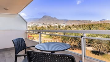 A balcony with two chairs and a table, overlooking a mountainous landscape and a golf course.