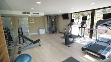 Un gimnasio con máquinas de cardio, bancos de pesas y un espejo grande.