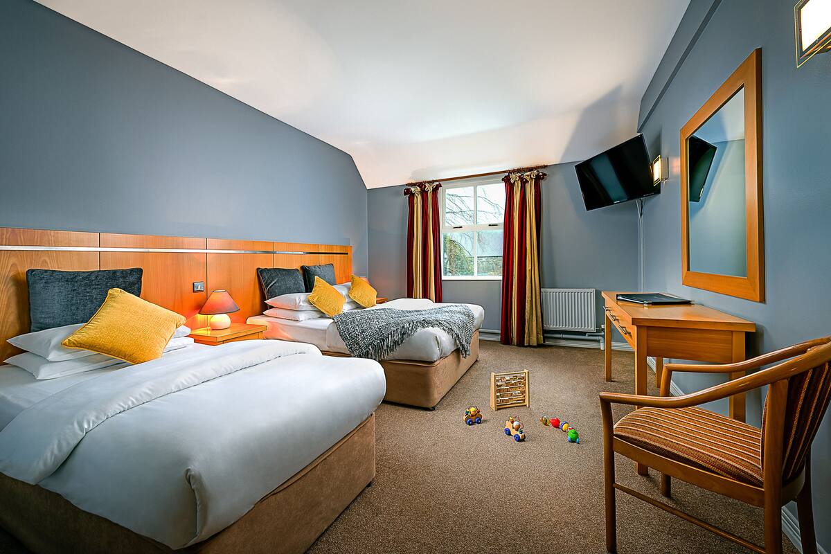 A hotel room with two beds, a desk, a chair, a TV, and toys on the floor.
