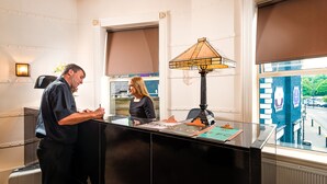 Una reception con una lampada, una finestra con persiane e vista sulla strada.