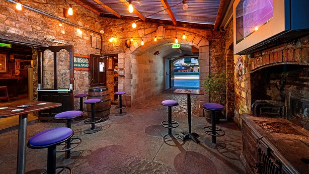 Un'area bar rustica con pareti in pietra, travi in legno e un camino in mattoni. Sono presenti diversi sgabelli e un bancone bar.